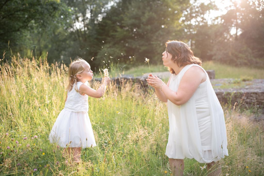 Séance photo en famille maman et sa fille soufflant des fleurs dans un champ en sarthe